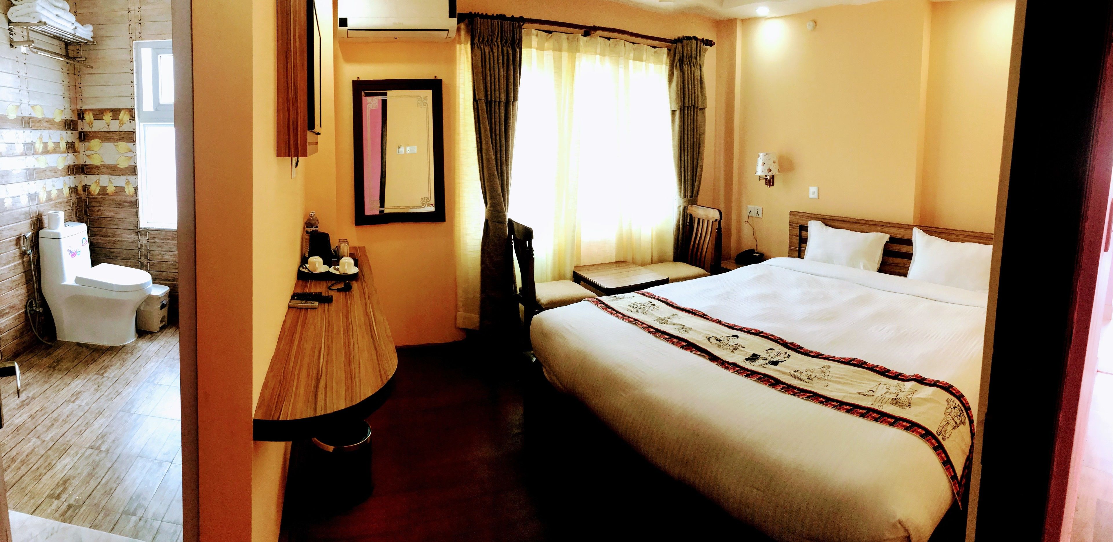 A hotel room with a large bed, a small table, a chair, a toilet, and a window with curtains.