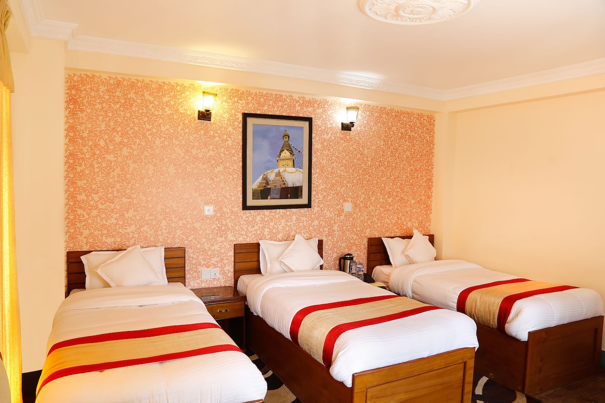 A hotel room with three single beds, a wooden headboard, a nightstand, and a framed picture on the wall.