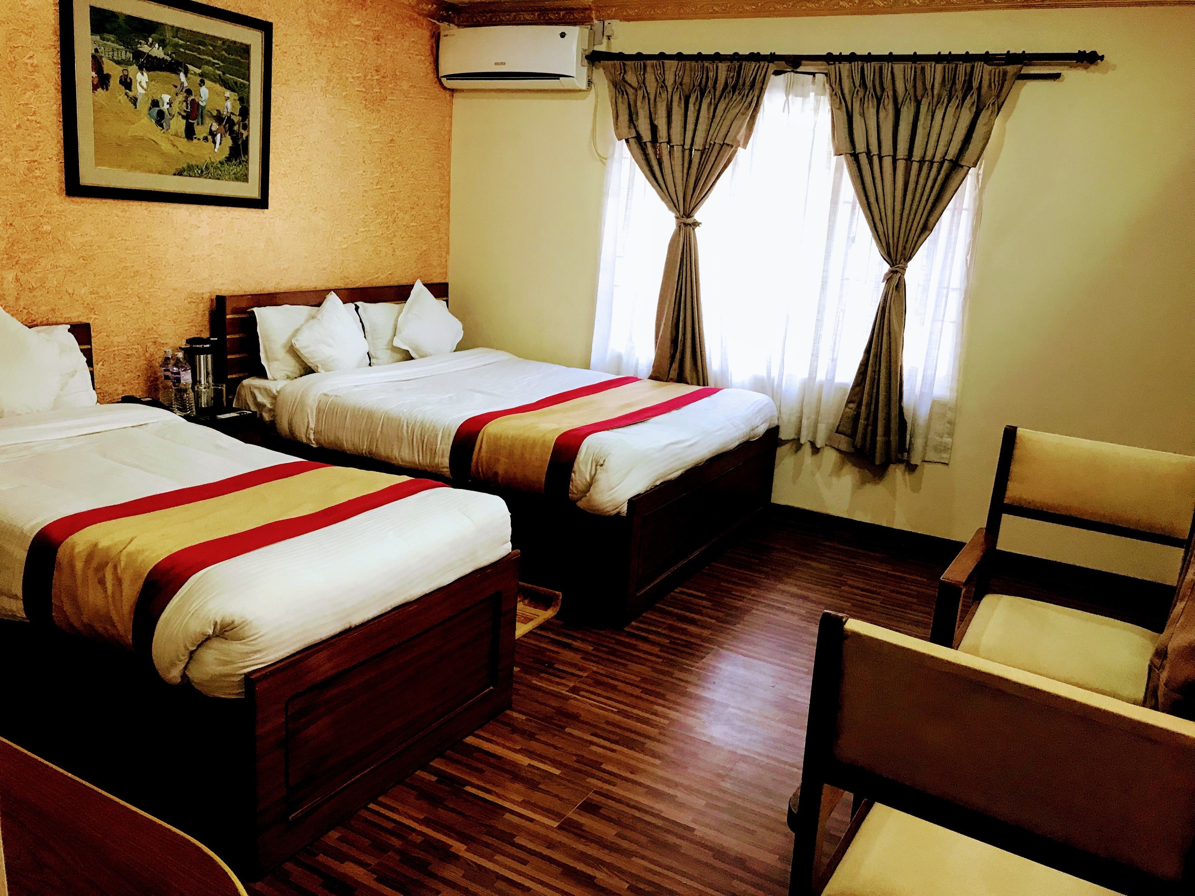 A hotel room with two beds, a wooden floor, a chair, and a painting on the wall.