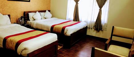 A hotel room with two beds, a wooden floor, a chair, and a painting on the wall.