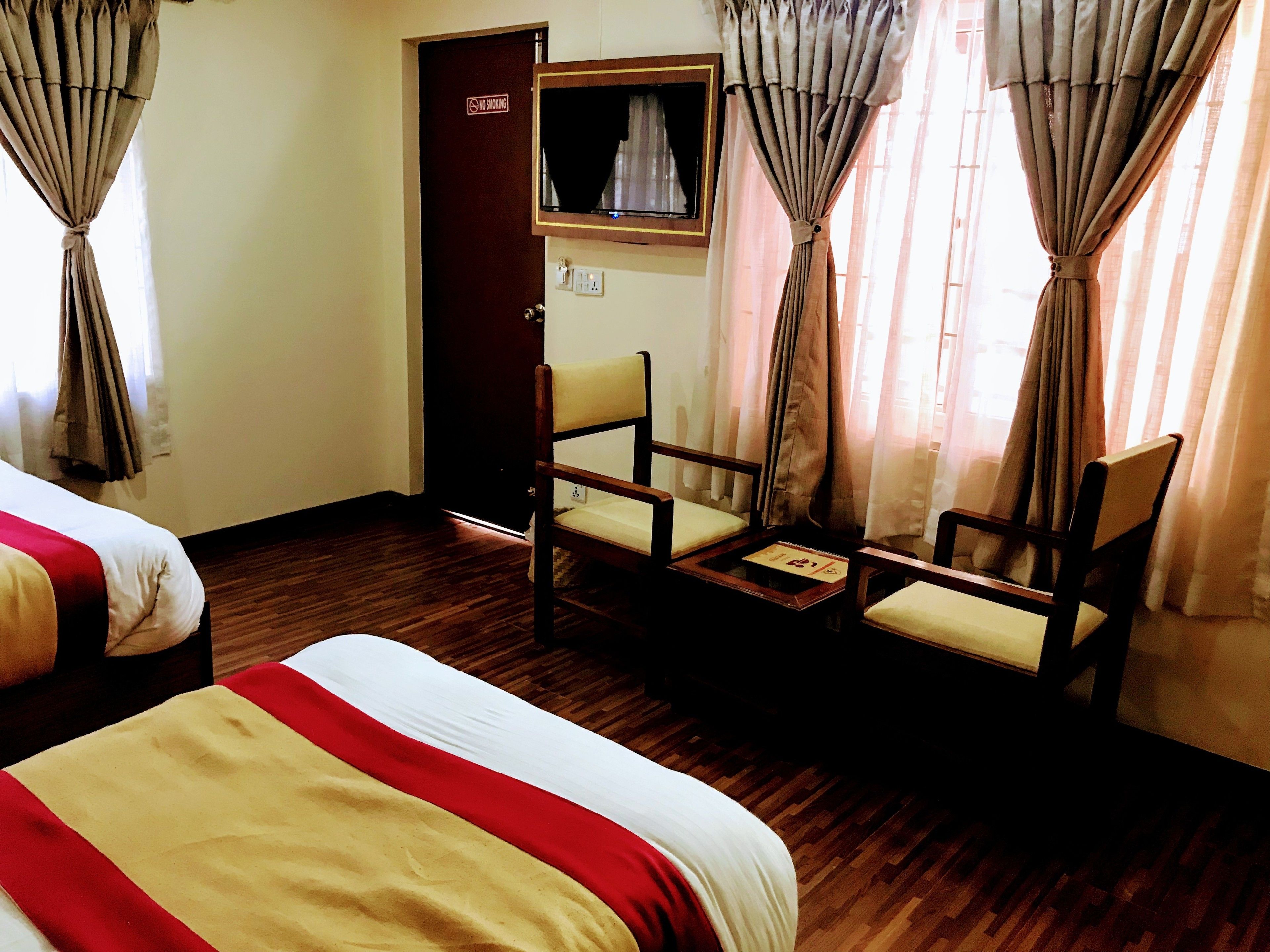 Une chambre d’hôtel avec deux lits, une chaise, une petite table et une porte sur laquelle est apposée une pancarte « Il est interdit de fumer ».