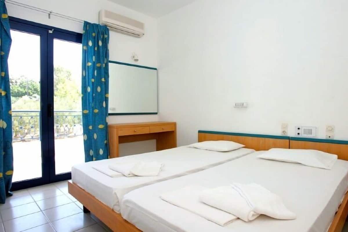 A hotel room with two beds, a wooden desk, a mirror, and a view of greenery outside.