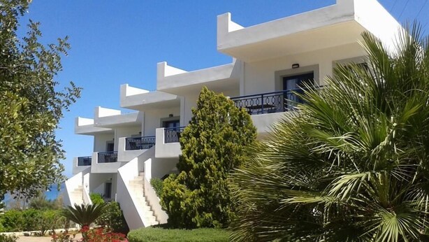 A modern white building with a staircase leading to a balcony, surrounded by greenery and a clear blue sky. - Irene Village (Hersonissos)