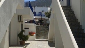 A narrow stone-paved alleyway flanked by white buildings with blue accents, leading to a staircase and a mountain in the background. - Irene Village (Hersonissos)