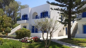 A modern building with white walls and blue accents, featuring a staircase and a small garden with flowers. - Irene Village (Hersonissos)