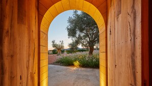 Ein gewölbter Holzeingang, der in einen Garten mit Baum und Blumen führt.