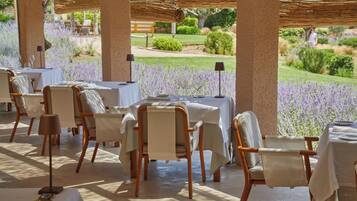 An outdoor dining area with tables and chairs, surrounded by a garden with lavender plants.