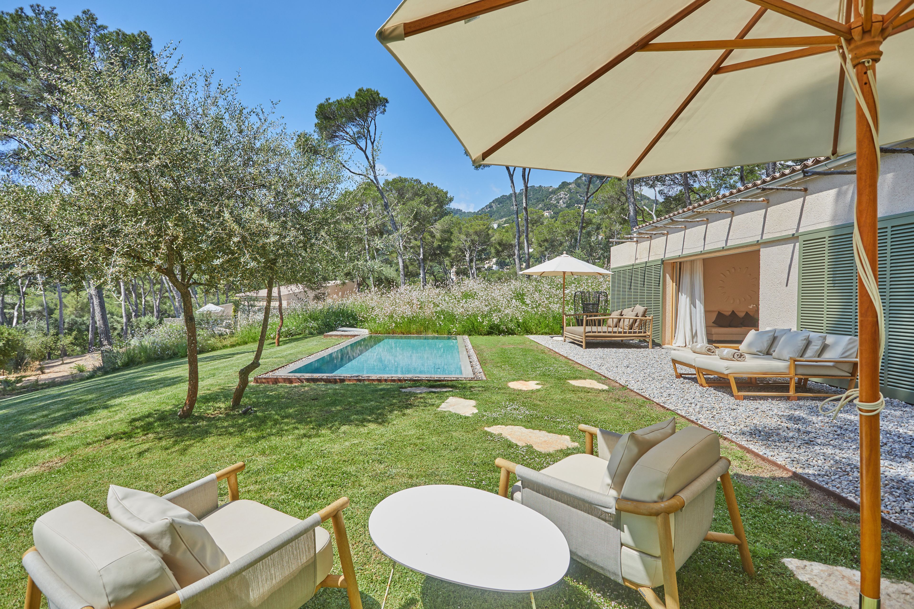 Zona junto a la piscina con mesa y sillas, un espacio de descanso cubierto y vistas a la piscina y vegetación circundante.