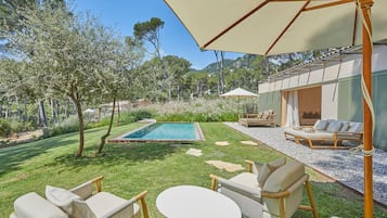 Zona junto a la piscina con mesa y sillas, un espacio de descanso cubierto y vistas a la piscina y vegetación circundante.