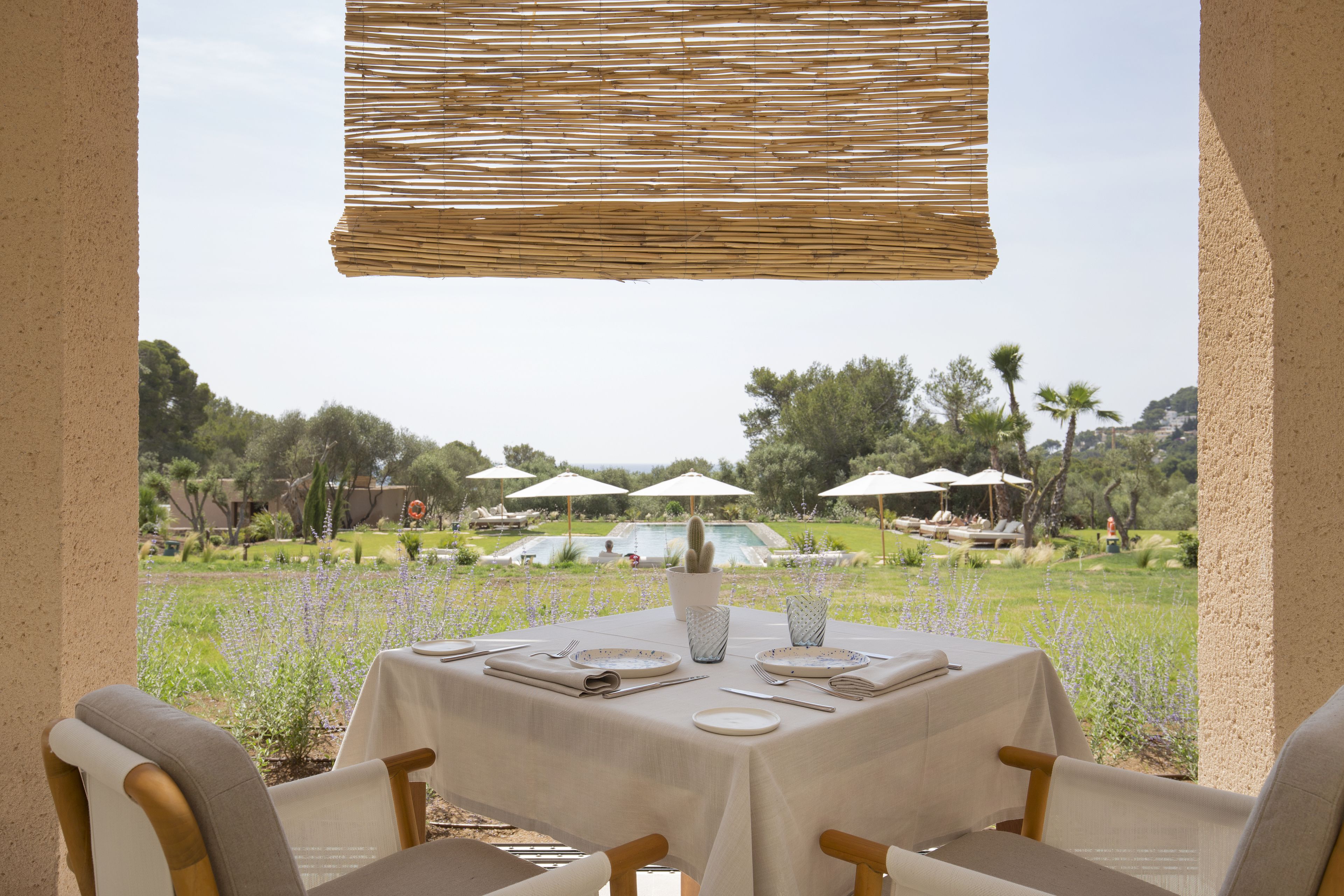 An outdoor dining area with a table set for two, surrounded by chairs, and overlooking a pool and garden.