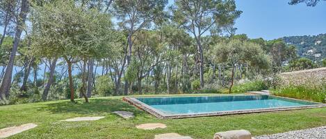 Un espace aménagé au bord de la piscine, avec une piscine rectangulaire entourée d’une pelouse et d’arbres. Des chaises longues et des serviettes sont à disposition.