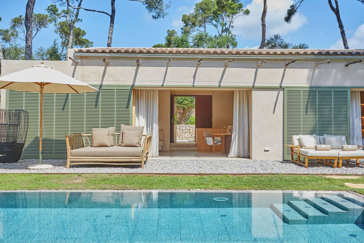 Un espace aménagé au bord de la piscine, comprenant une piscine, du mobilier d’extérieur et un bâtiment doté de volets.