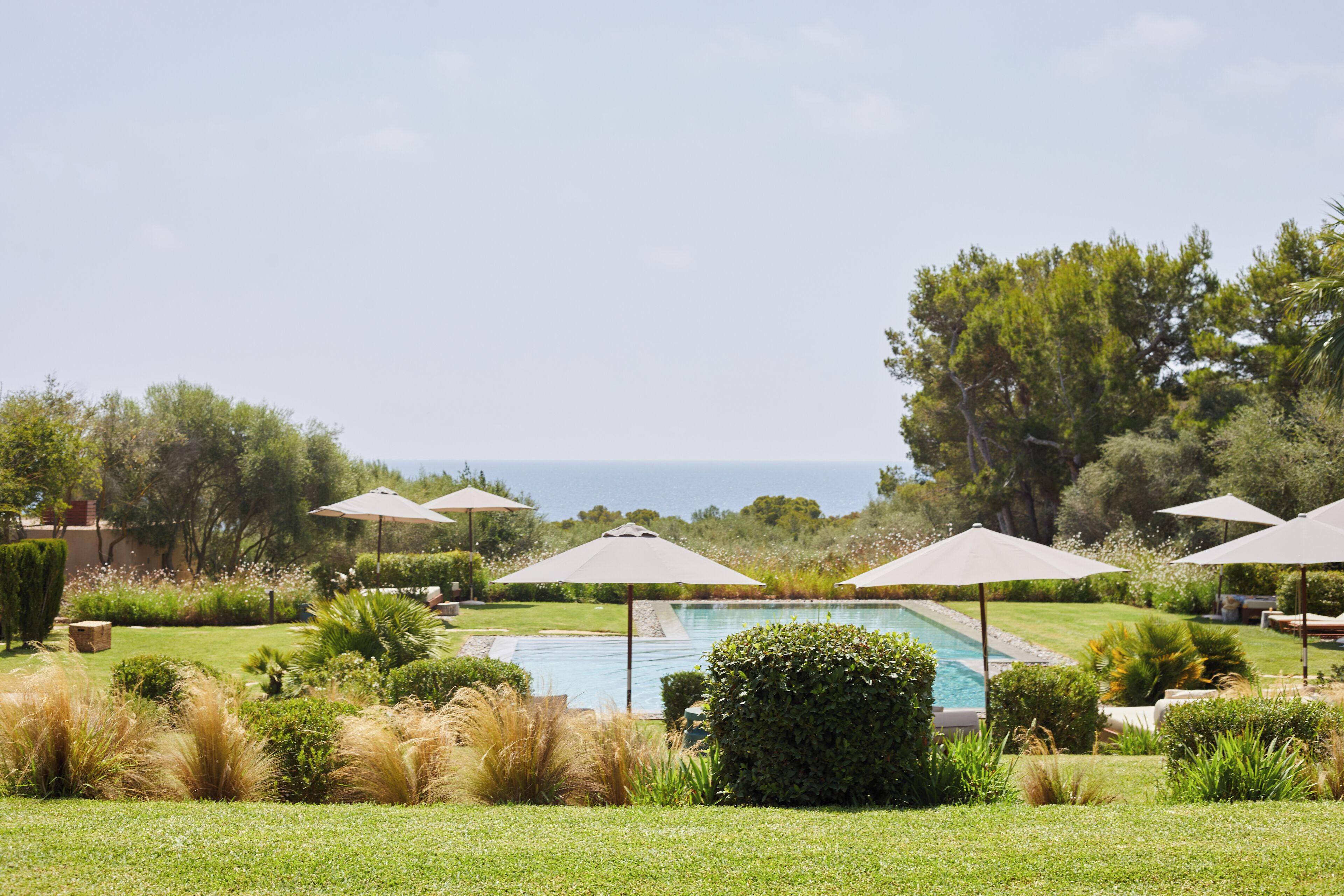 Zona de piscina con sombrillas, abundante vegetación y vista al mar.