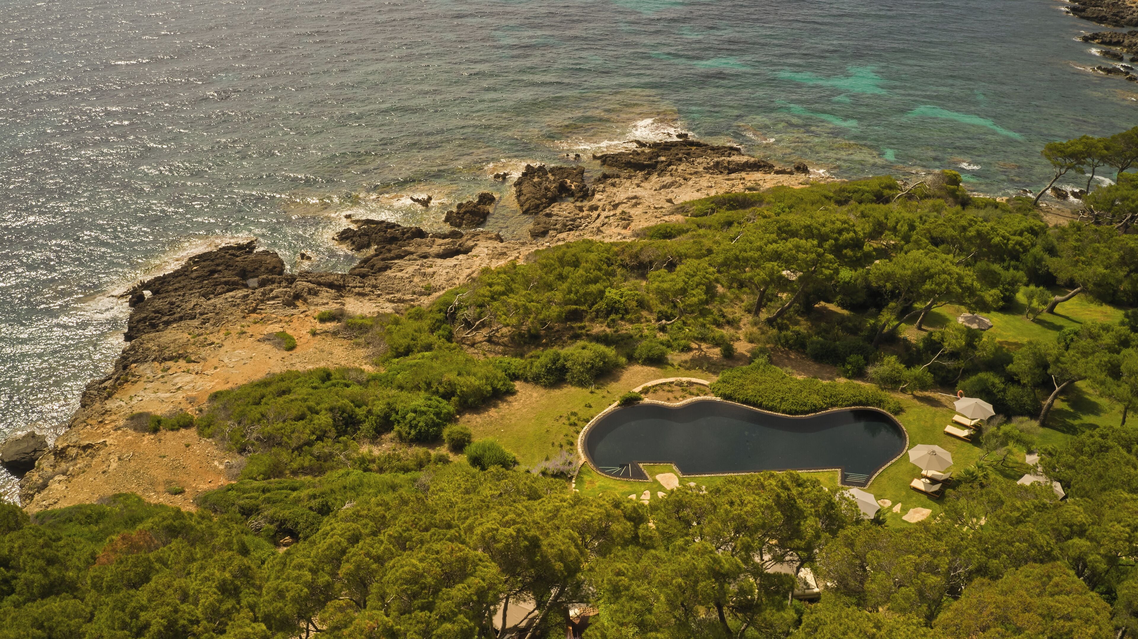 Vista aérea de una zona costera con piscina rodeada de abundante vegetación y terreno rocoso.