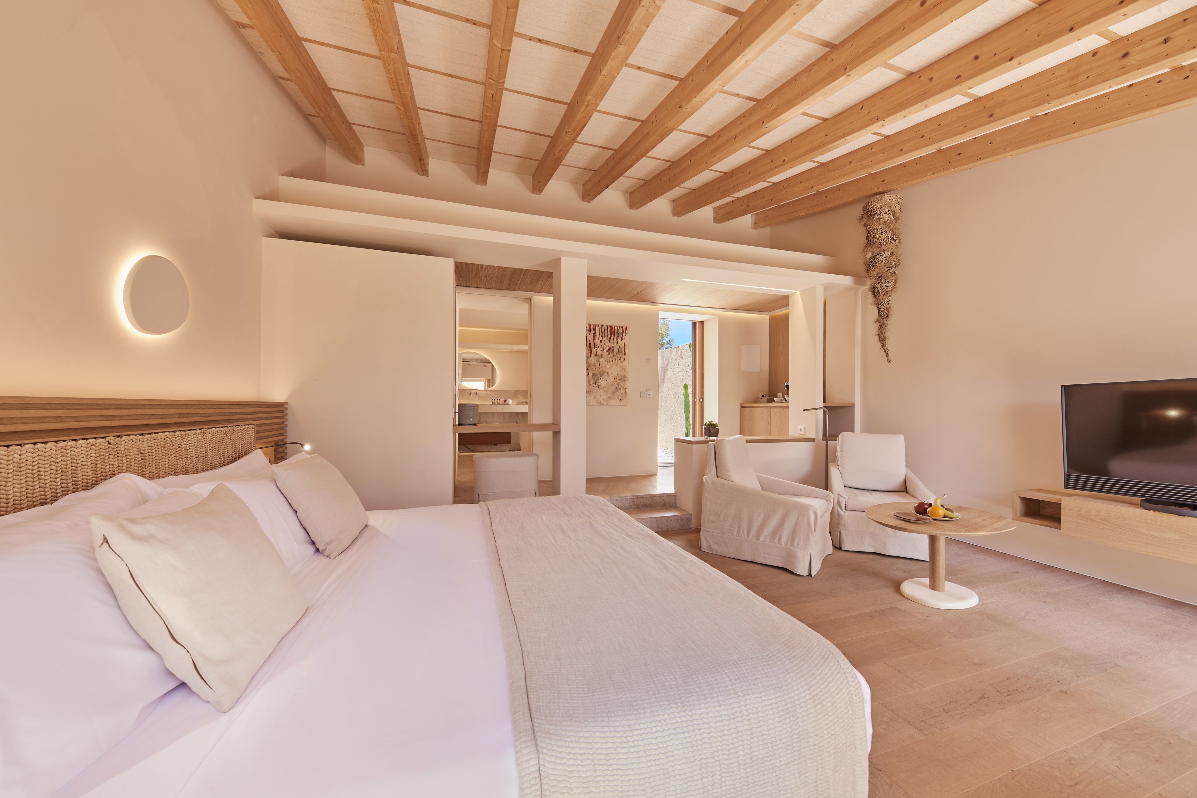 Una habitación de hotel moderna con una cama grande, televisión, zona de estar y un baño visible a través de una puerta abierta.