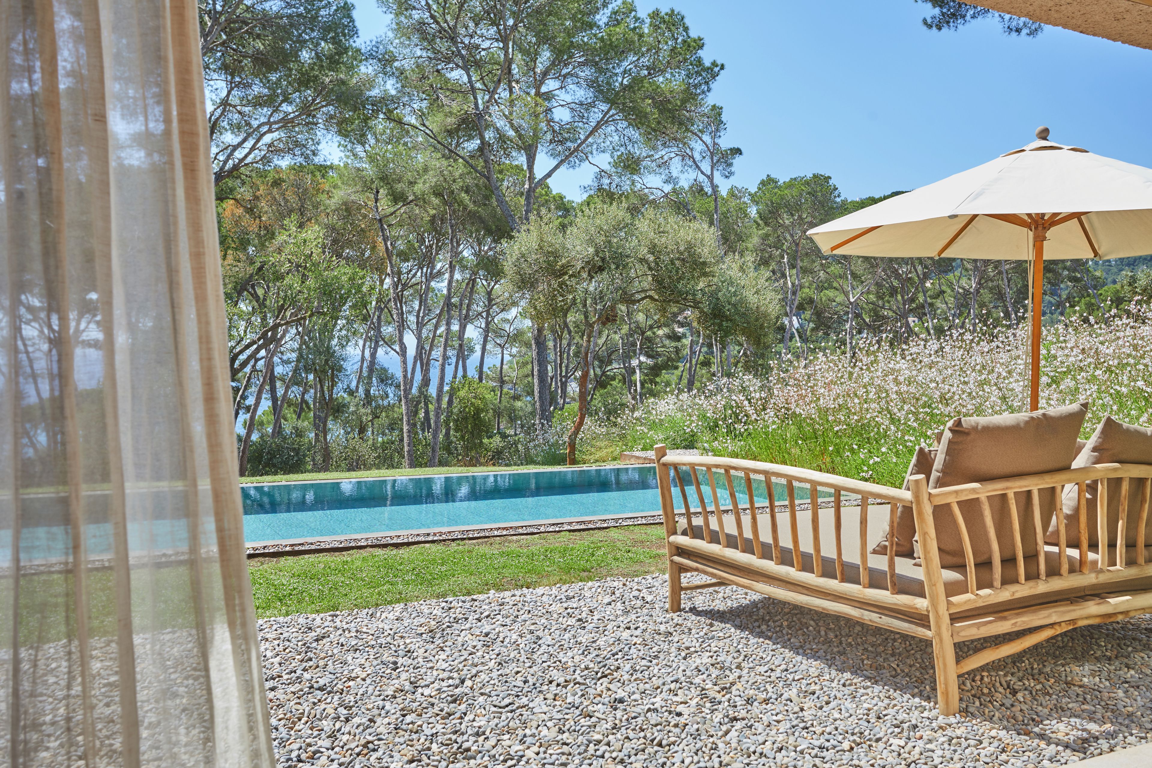Un banco de madera con cojines, una piscina y vistas a árboles.