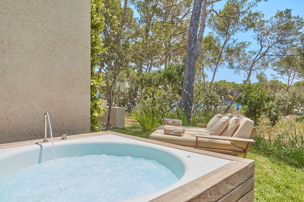 Un espace de détente avec un jacuzzi entouré de verdure et une chaise longue.