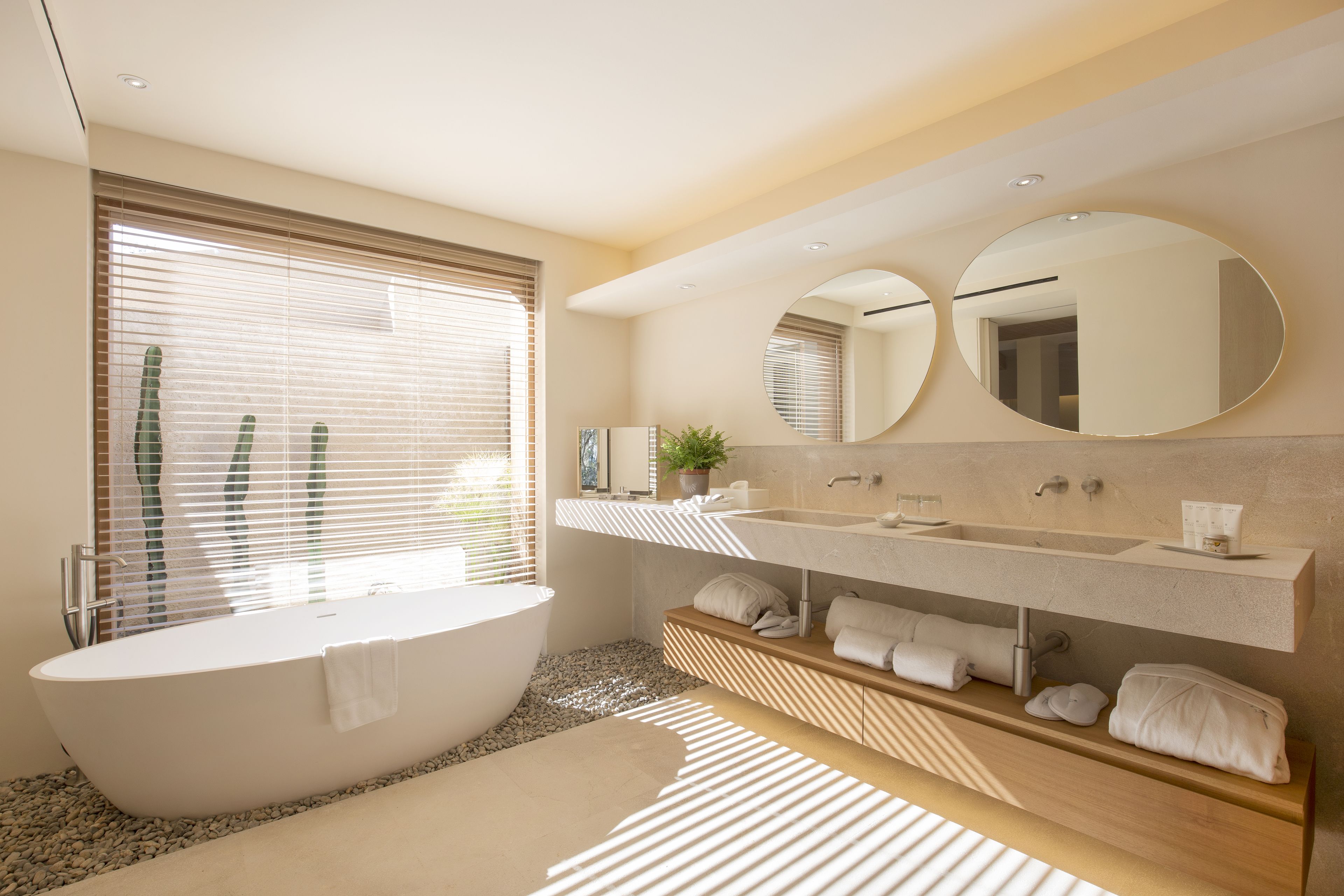 A modern bathroom with a freestanding bathtub, a vanity with a mirror, and a shelf with towels.