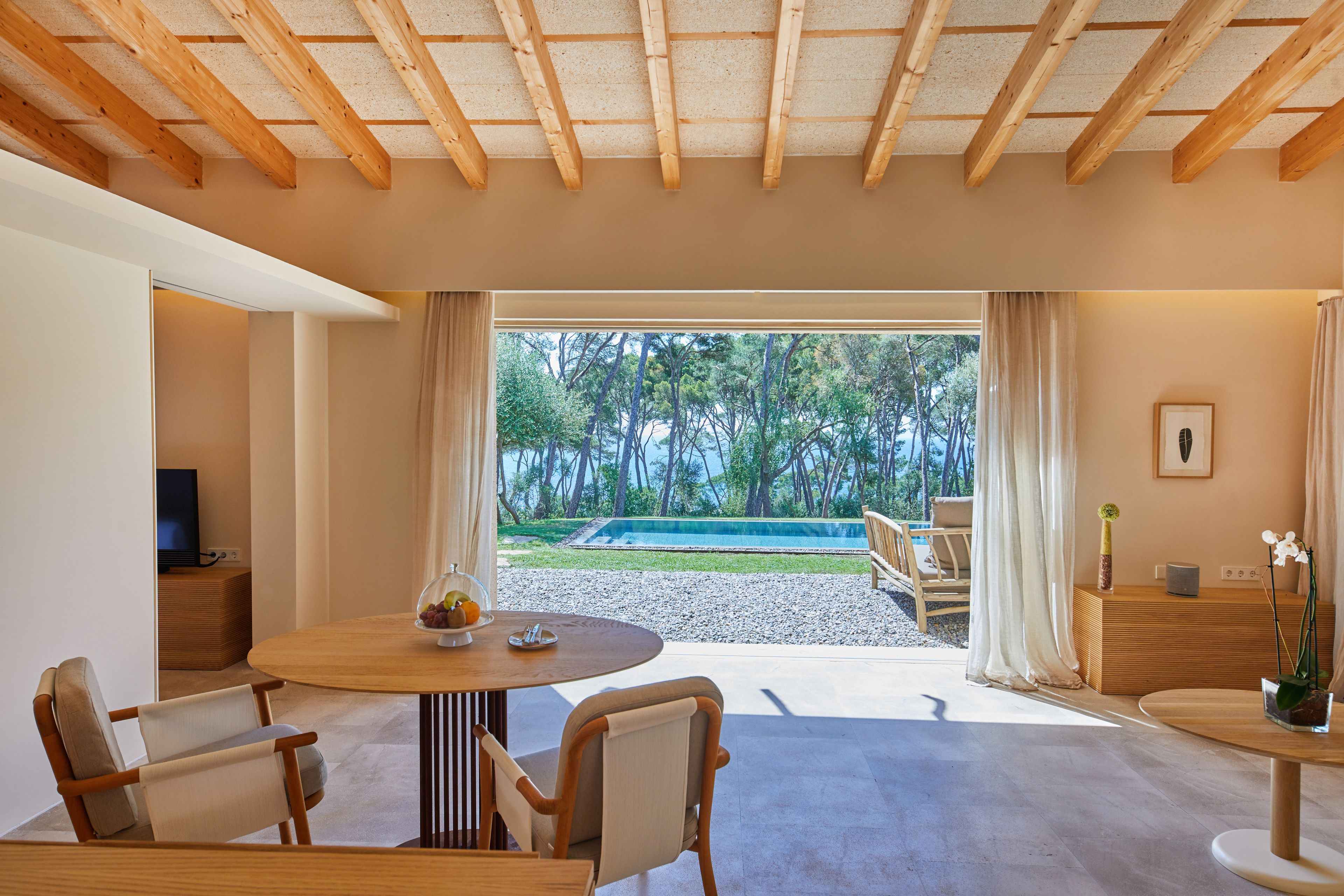 Ein modernes Interieur mit Essbereich, Fernseher und Blick auf Pool und Bäume.
