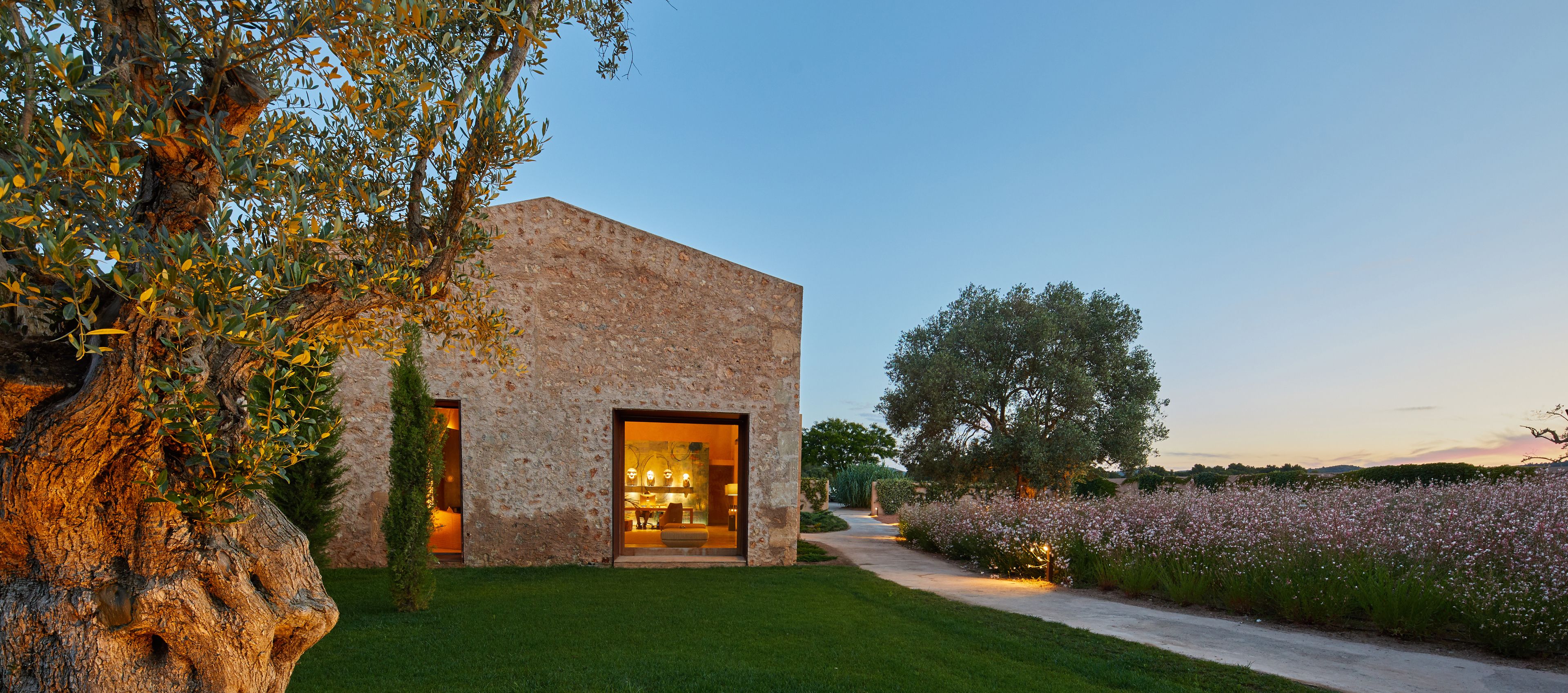 Un bâtiment rustique en pierre, doté d’une grande porte ouverte et d’un jardin bien entretenu.