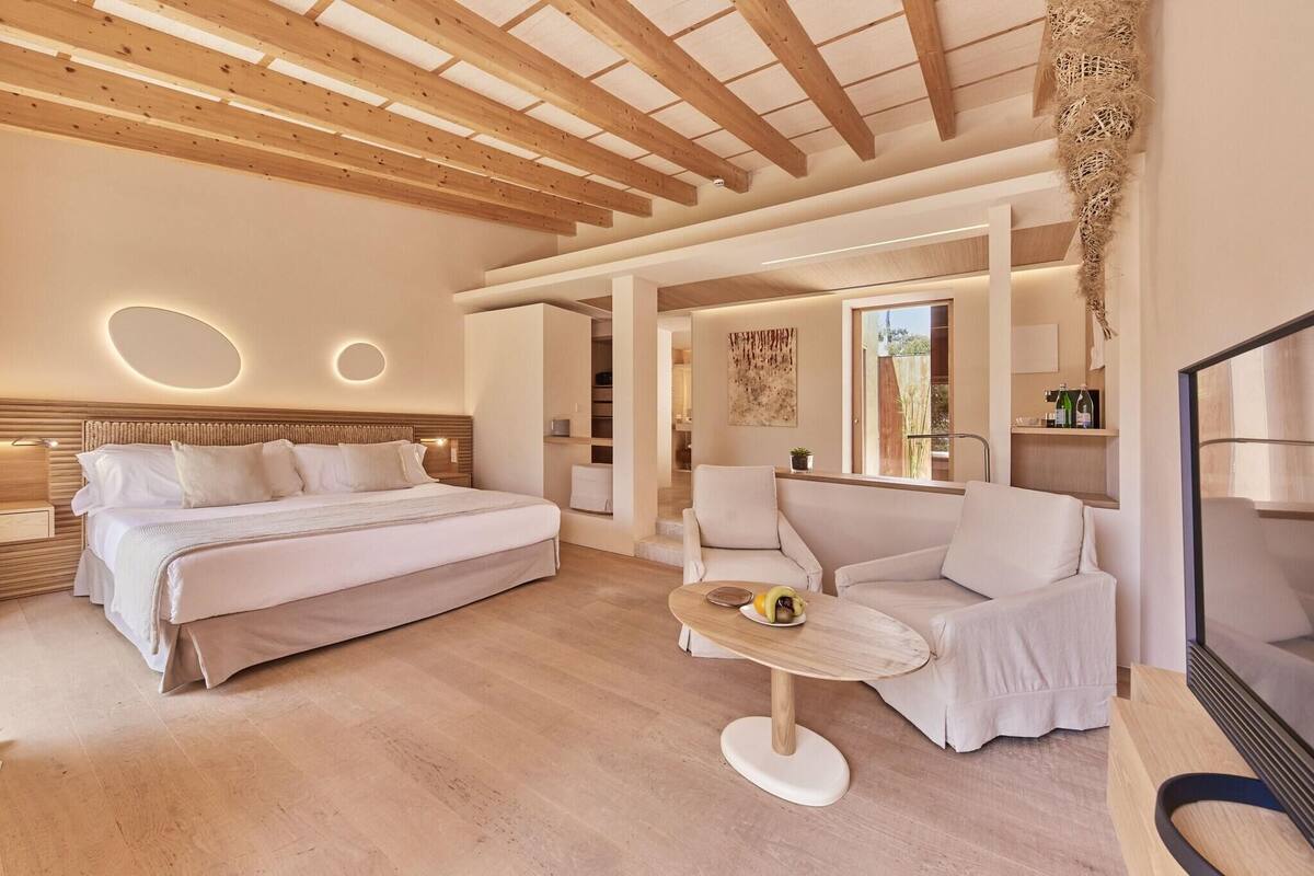 Une chambre d’hôtel moderne avec un plafond en bois, un grand lit, un canapé et une petite table sur laquelle sont disposés des fruits.