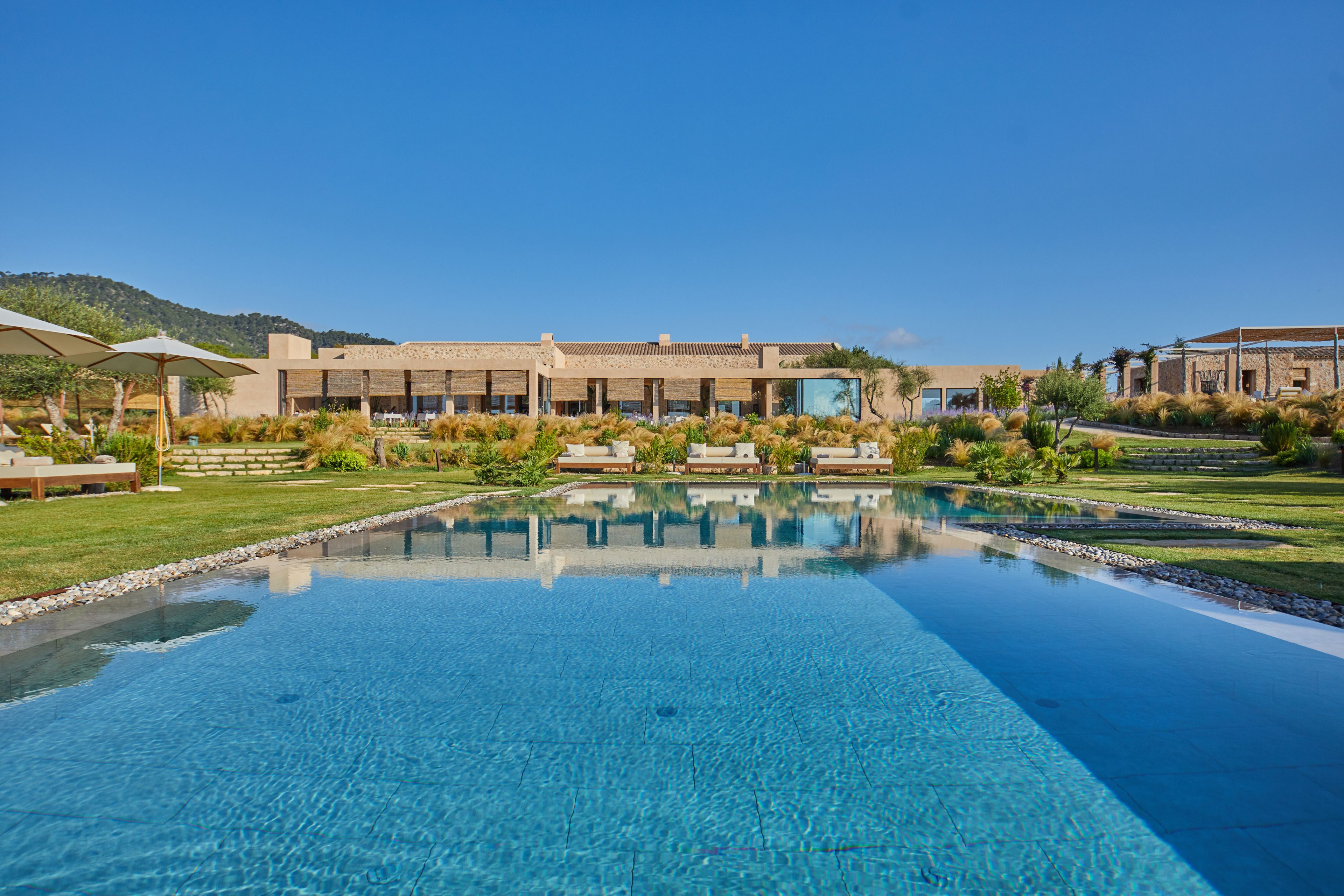 Un hotel moderno con una amplia piscina infinita, mobiliario exterior y vistas a las montañas.