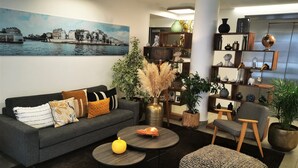 Un salon moderne avec un canapé gris foncé, une table basse ronde et un grand tableau représentant un paysage urbain.