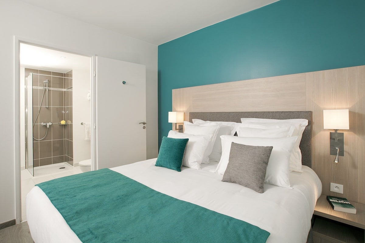 Una habitación de hotel con una cama, ducha y una mesita de noche con lámpara.