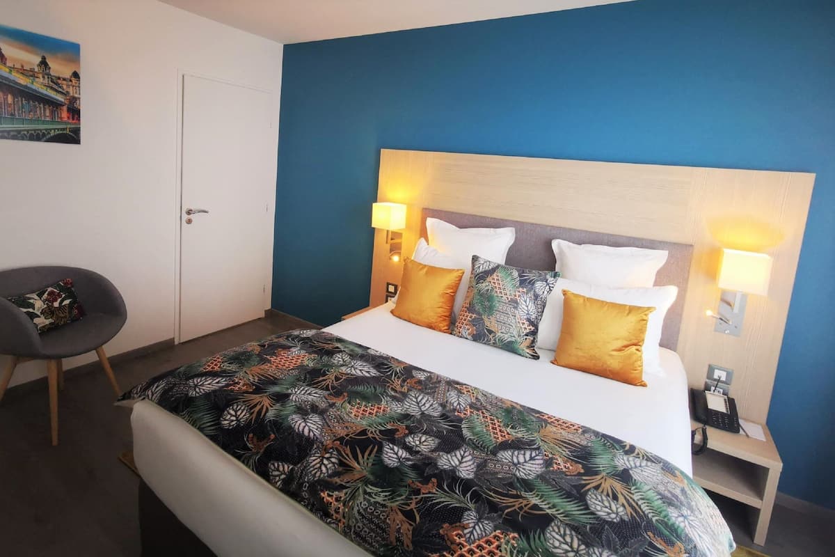 Una habitación de hotel con una cama, dos mesitas de noche, una silla y un cuadro en la pared.