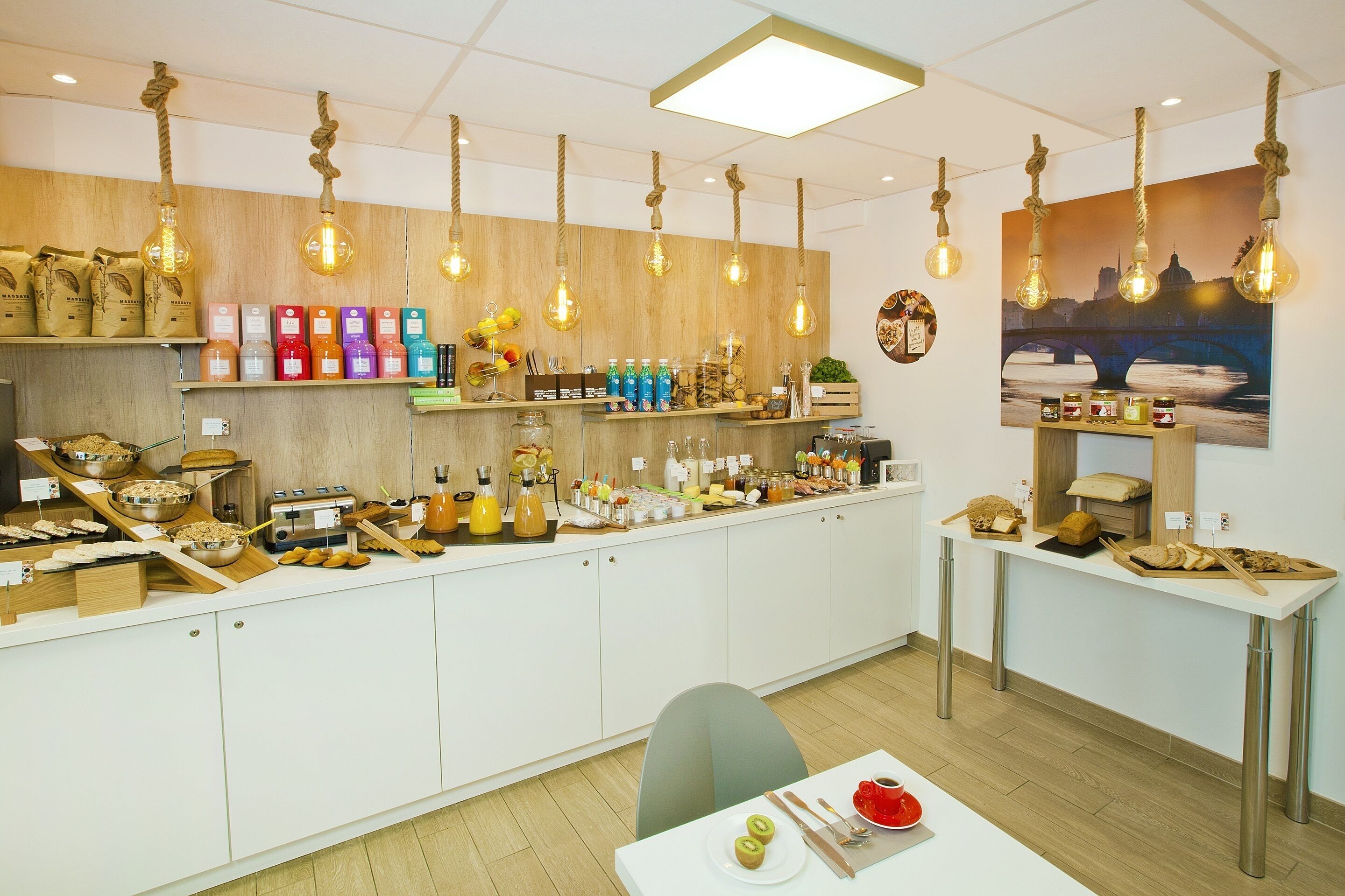 A cafe with a long counter, various food items, and hanging light bulbs.