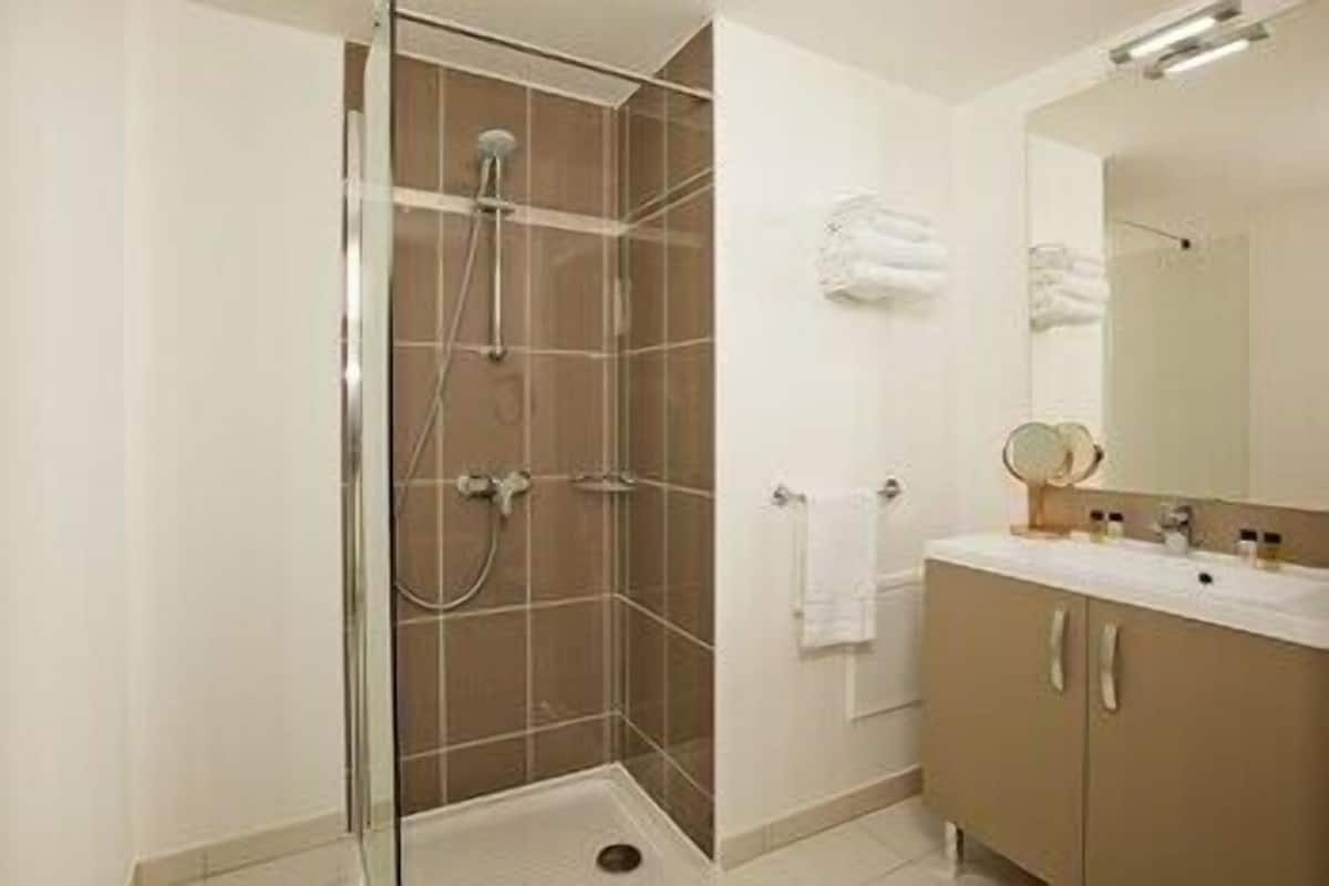Un baño con ducha envuelta en vidrio, un lavamanos con espejo y un perchero para toallas.