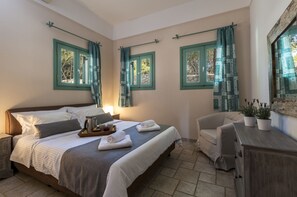 A well-lit bedroom with a large bed, two windows with curtains, a bedside table with a lamp, a chair, and a dresser. - Electra Beachfront Villa (Ermionida)