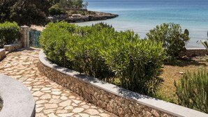 A stone pathway leading to a coastal view with a clear sky and distant mountains. - Electra Beachfront Villa (Ermionida)