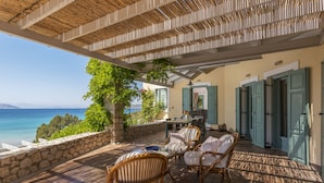 An outdoor patio with wicker furniture, a stone wall, and a view of the sea. - Electra Beachfront Villa (Ermionida)