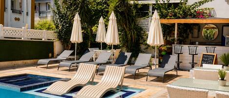 A poolside area with lounge chairs, umbrellas, and a signboard listing amenities.