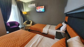 Hotellihuone, jossa on kaksi sänkyä, seinälle asennettu televisio, tuoli ja ilmastointilaite.