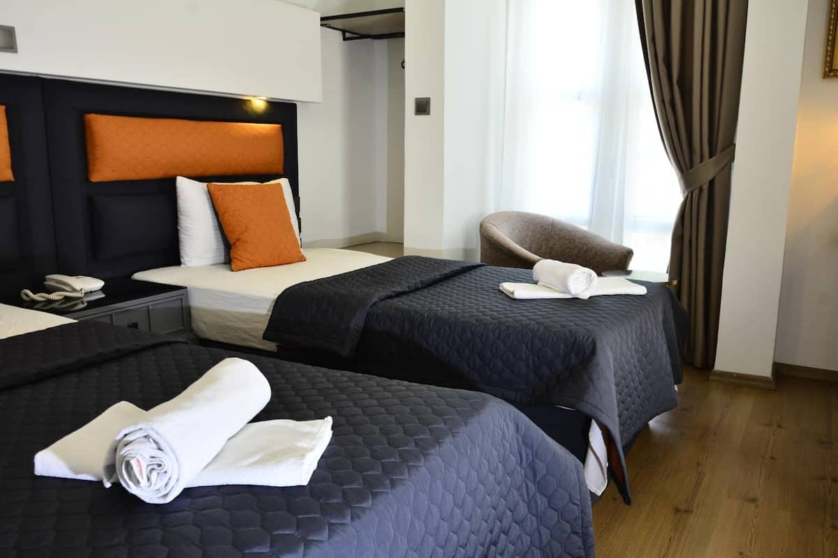 Une chambre d’hôtel avec deux lits, une chaise, un bureau avec un téléphone et une fenêtre avec des rideaux.