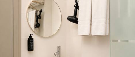 A bathroom with a round mirror, a towel rack, a sink, and a bottle of shampoo.