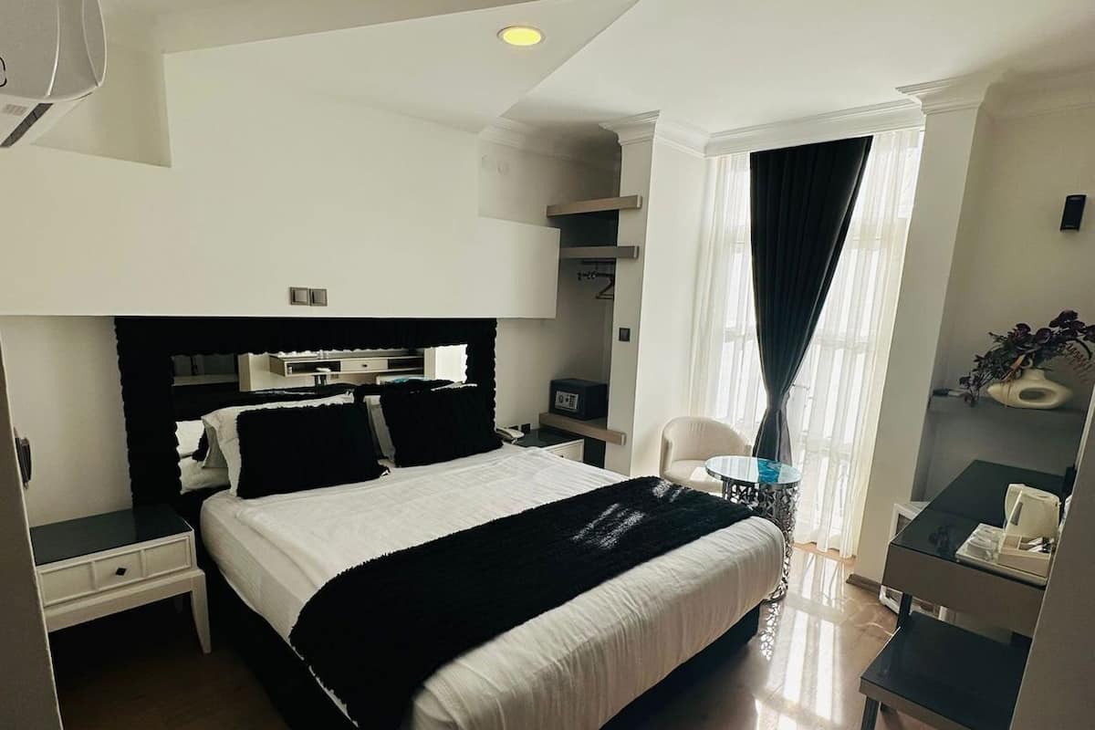 Une chambre d’hôtel avec un grand lit, un bureau, une chaise et une fenêtre avec des rideaux.