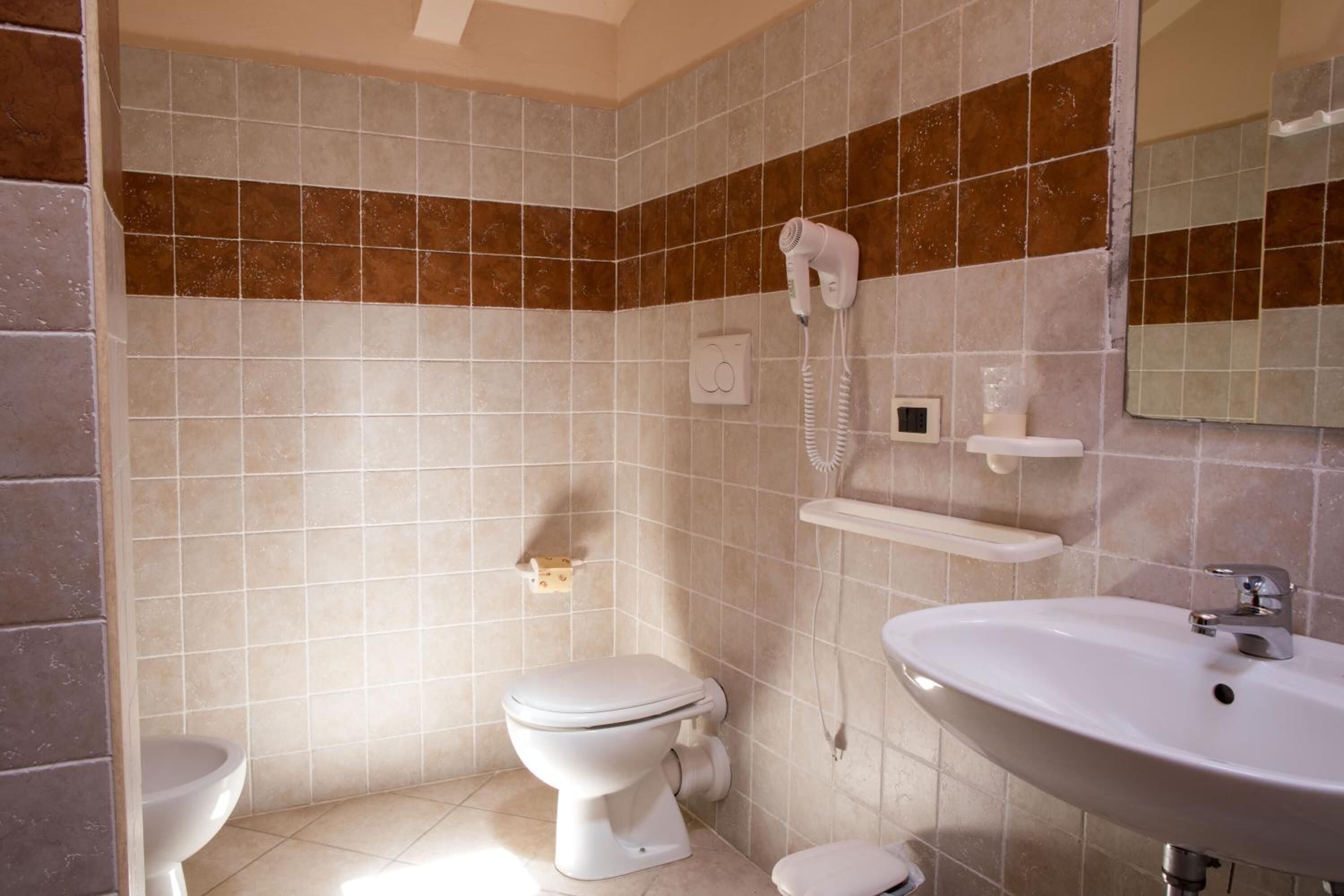 Un baño con inodoro, lavamanos y secador de pelo fijado en la pared.