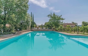 A rectangular swimming pool with a clear blue water surface, surrounded by trees and a stone wall. - Borgo Nuovo San Martino (Bucine)