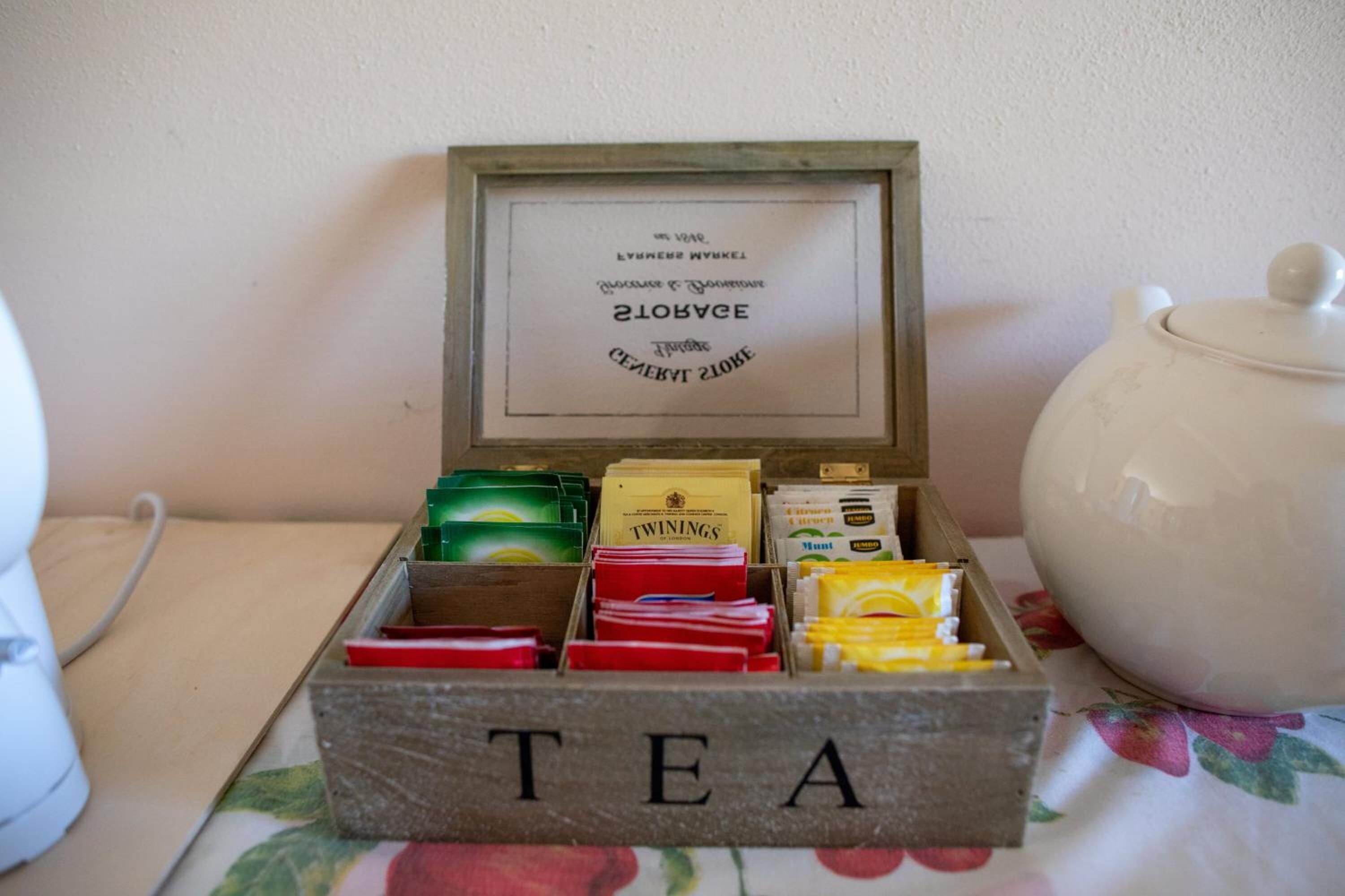 Una caja de té con compartimentos que contienen diferentes marcas de té y un certificado enmarcado encima.