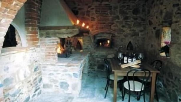Une pièce aux murs de pierre, avec une cheminée, une table entourée de chaises et un luminaire suspendu.