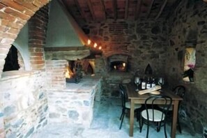 A stone-walled room with a fireplace, a table with chairs, and a hanging light fixture. - Borgo Nuovo San Martino (Bucine)