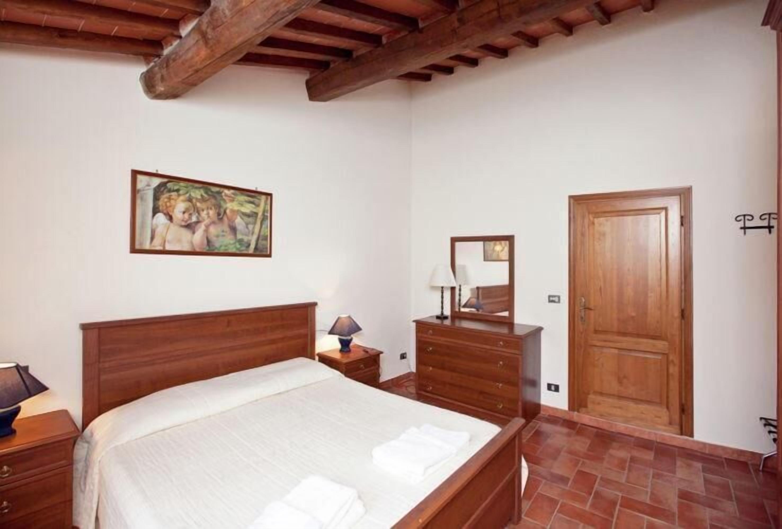 Un dormitorio con cama de madera, mesita de noche, cómoda, espejo y puerta.