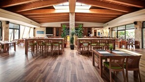 Un comedor amplio con mesas y sillas de madera, un pilar central y ventanas grandes que dejan entrar luz natural.