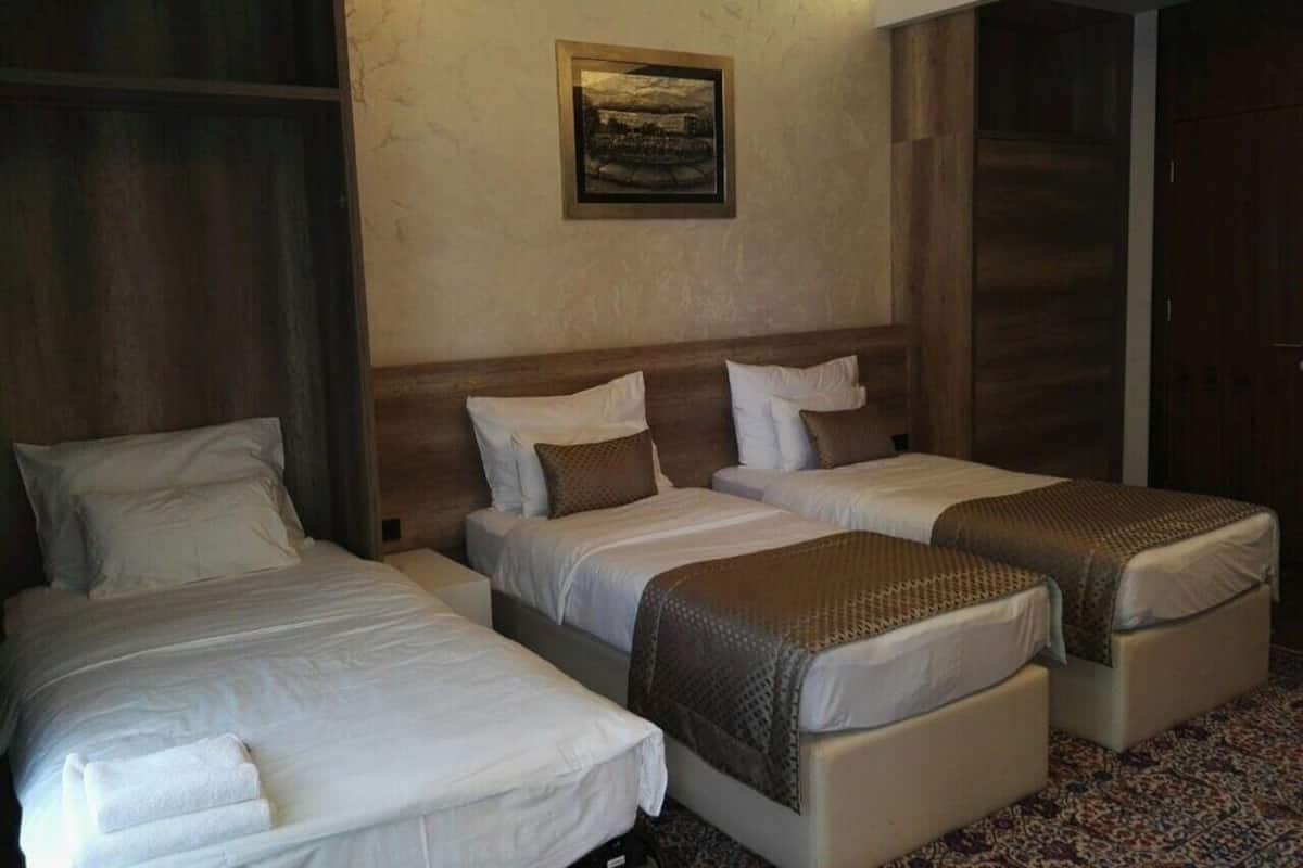 Habitación de hotel con tres camas, cabecera de madera, un cuadro enmarcado en la pared y alfombra estampada.