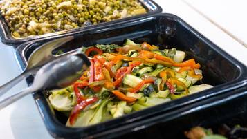 Un bufé con diversos platos, incluyendo una ensalada de verduras variadas y un recipiente con cereales mezclados.