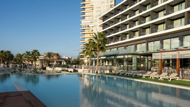 Un hotel con piscina, palmeras y un edificio moderno con balcones.