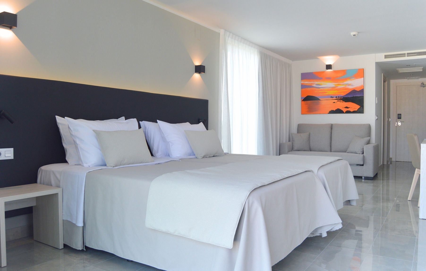 Una habitación de hotel moderna con una cama grande, un sofá, un escritorio y un cuadro en la pared.